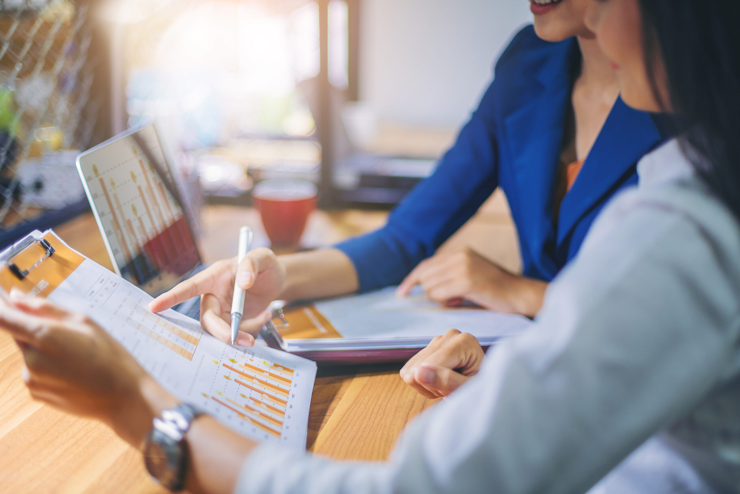 Zwei Geschäftspersonen analysieren Diagramme und Daten auf Papier und Laptop bei einer Besprechung.